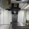 A 4th axis rotary table bolted to the right-hand end of a vertical machining center table, with the spindle above