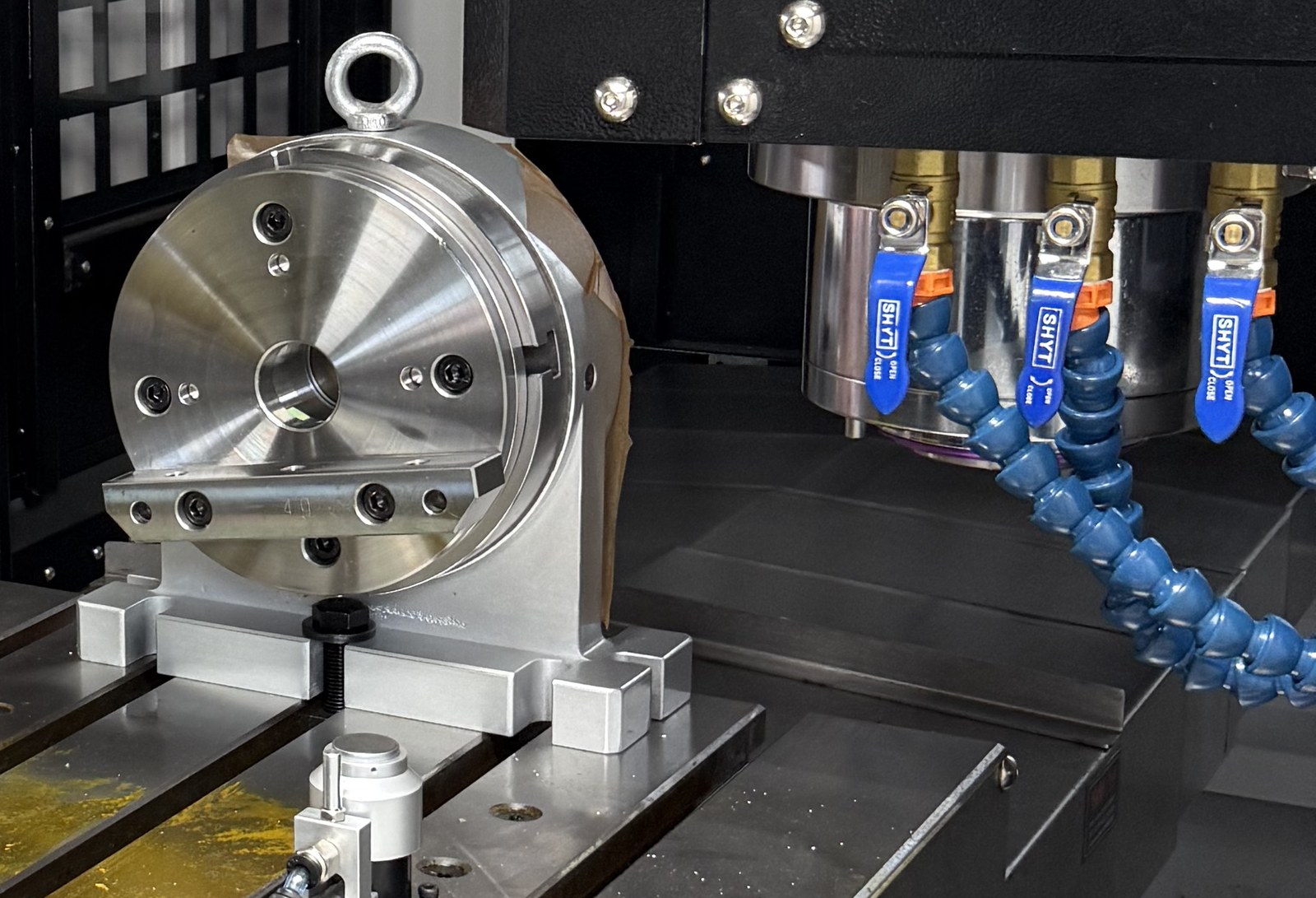 Round faceplate-type tailstock clamped in the T-slots of a VMC table, with the spindle and coolant nozzles behind it