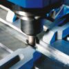 A friction stir welding tool running along the joint between two clamped aluminum plates, leaving a fresh weld seam behind it