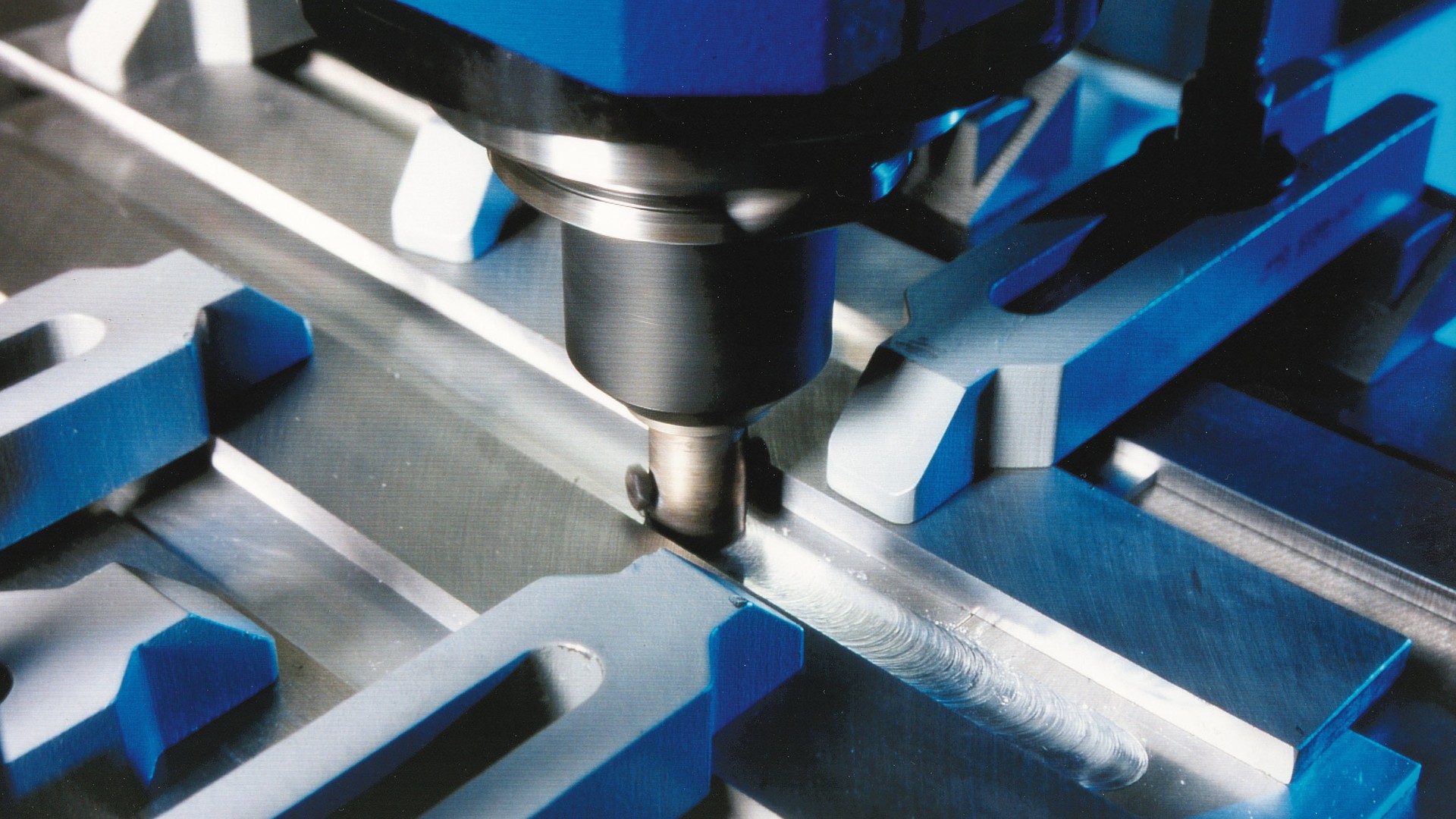A friction stir welding tool running along the joint between two clamped aluminum plates, leaving a fresh weld seam behind it