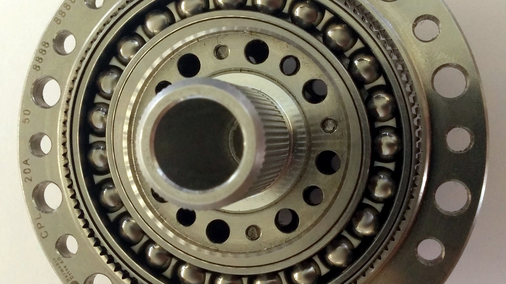 Close-up of an open strain wave gear, showing the bolted flange of the circular spline, the bearing balls and the central hub