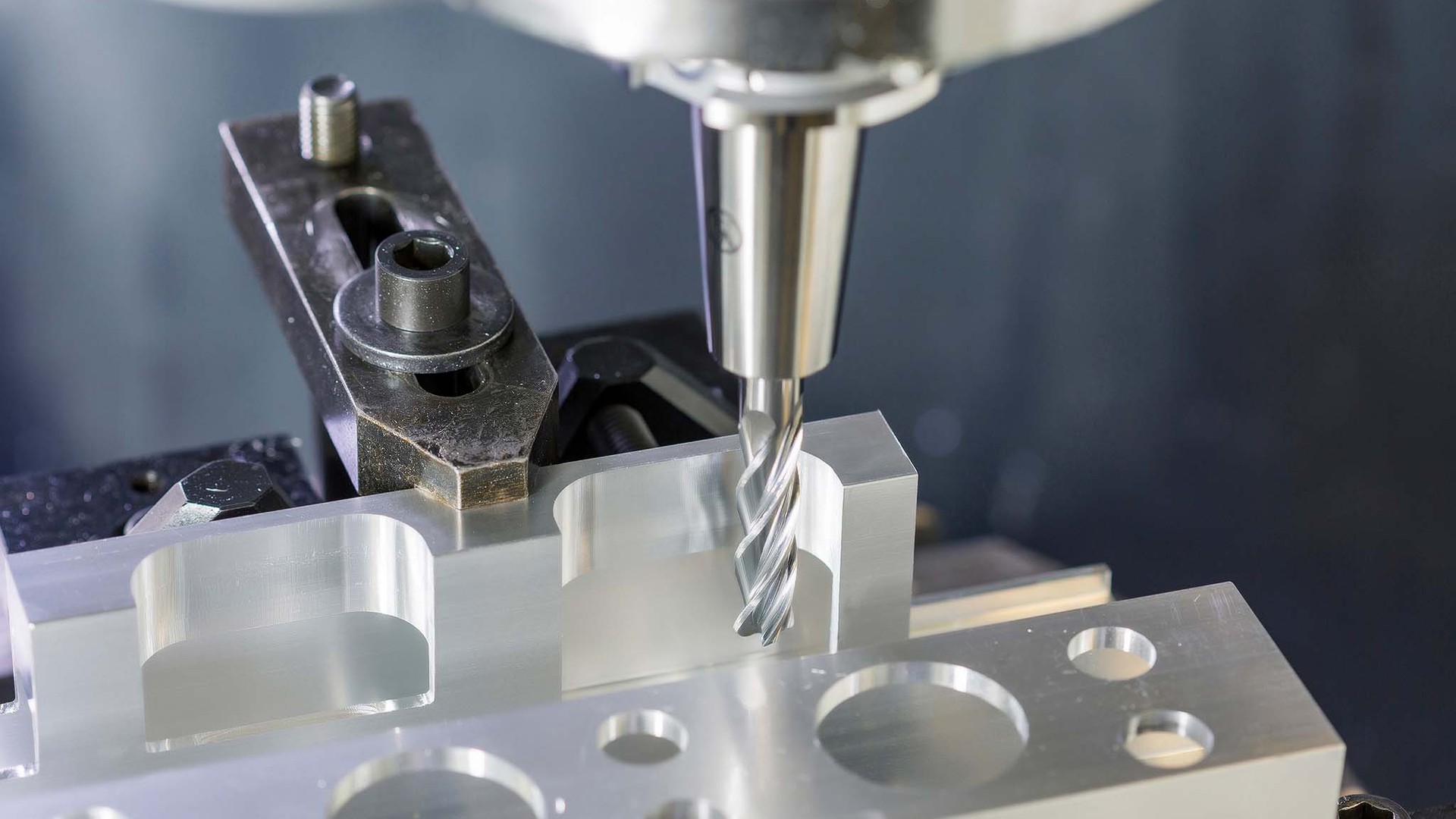 A solid carbide end mill machining holes and pockets in an aluminum battery frame test part clamped on a machine table